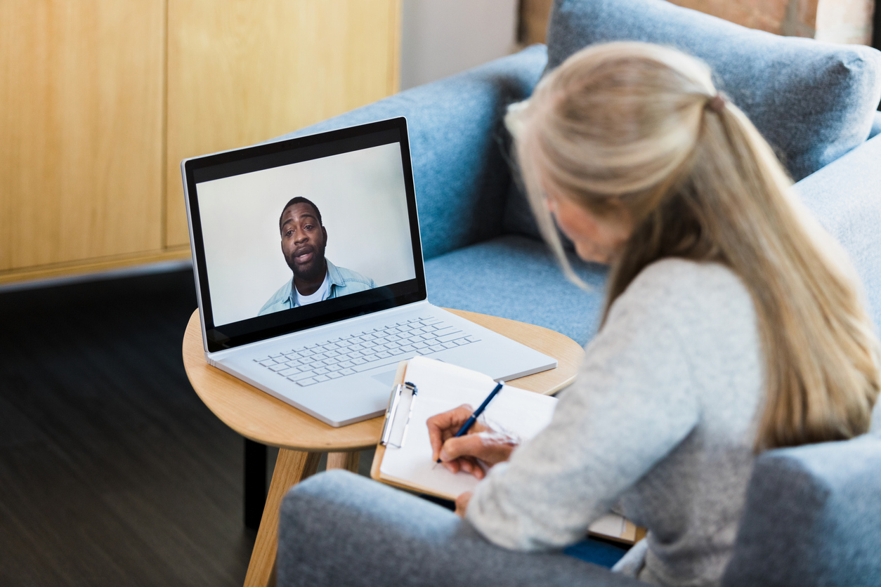 While teleconferencing, counselor takes notes as patient shares